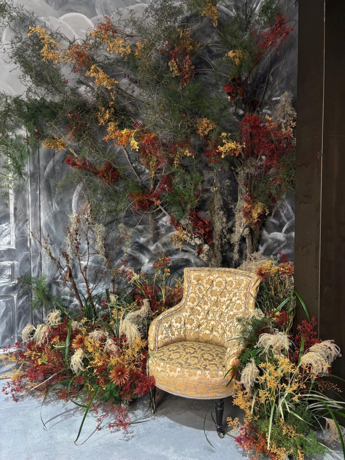 Escenografía floral de otoño con ramas, flores secas y una butaca vintage